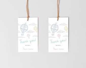 May include: Two white gift tags with a hot air balloon design. Each tag has a light blue, yellow, and pink hot air balloon illustration, with the words "Thank you!" and space for a name. The tags are suspended by brown twine.