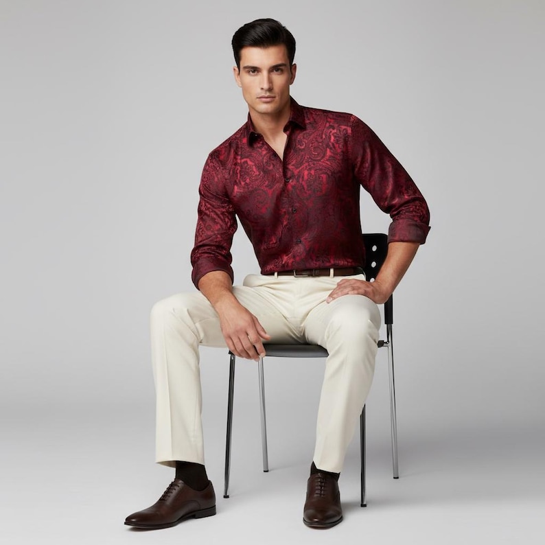 May include: A burgundy long-sleeve shirt with a paisley pattern. The shirt is paired with cream-colored pants, a brown belt, and brown leather shoes. The person is seated on a black chair.