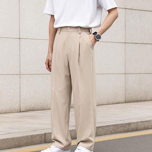 May include: Beige pleated trousers with a high waist and wide leg. The pants are paired with a white t-shirt. The trousers are made of a lightweight fabric and have a classic, tailored look.