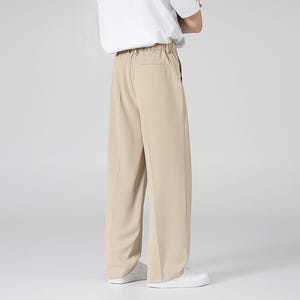 May include: Tan wide-leg pants with a relaxed fit. The pants have a high waist and a simple design, suitable for casual or semi-formal wear. The model is wearing a white t-shirt and white sneakers.