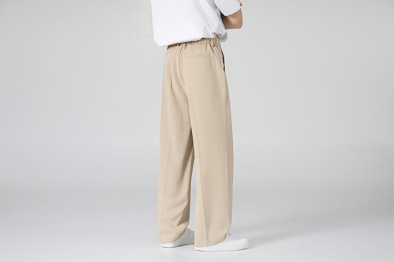 May include: Tan wide-leg pants with a relaxed fit. The pants have a high waist and a simple design, suitable for casual or semi-formal wear. The model is wearing a white t-shirt and white sneakers.