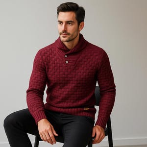 Peut inclure: Un pull bordeaux avec un col châle et un motif tissé texturé. Le pull a deux boutons au col et des manches longues. La personne porte un pantalon noir.