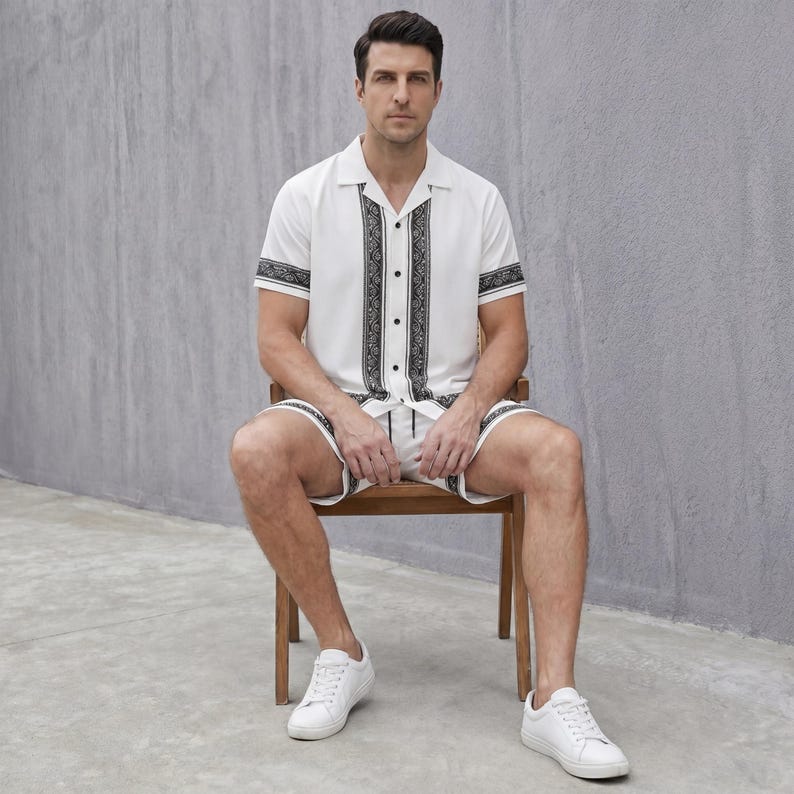May include: A white short-sleeved shirt and matching shorts set with black decorative patterns. The shirt has a collared neckline and button-up front. The shorts have a drawstring waist. The person is wearing white sneakers.