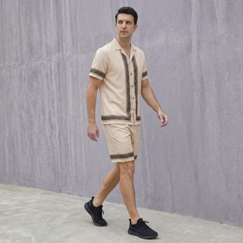 May include: A beige short-sleeved shirt and matching shorts set. The shirt has a collared neckline and decorative vertical panels. The shorts have a matching decorative border. The person is wearing black athletic shoes.