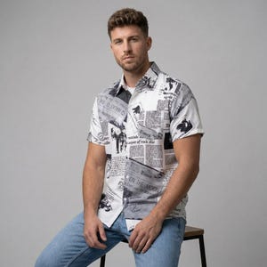 Puede incluir: Una camisa blanca de manga corta con estampado de periódico en blanco y negro. La camisa presenta varios titulares y artículos, incluido el texto "Times" y "ON THE MOON". La camisa se usa con jeans azul claro.