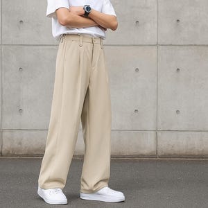 May include: A person wearing a white t-shirt and beige wide-leg pants. The pants have a pleated front and a relaxed fit. The person is also wearing white sneakers and a watch.