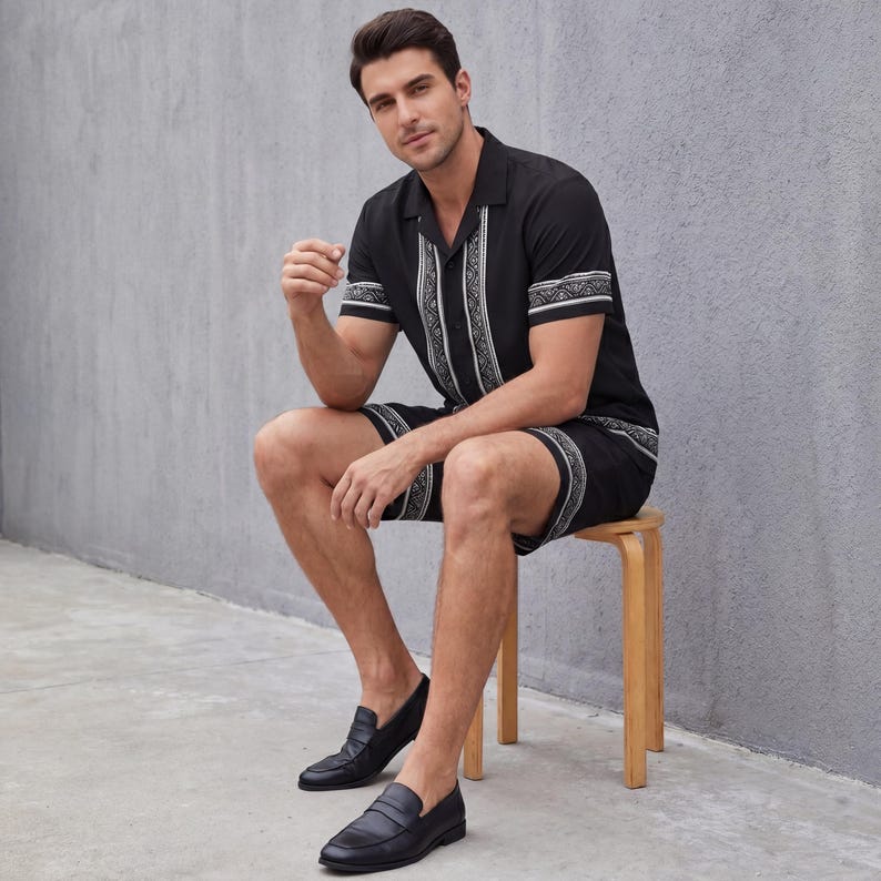 May include: Black short-sleeve shirt and shorts set with white geometric trim. The shirt has a collared neckline and the shorts have an elastic waistband. The model is wearing black leather loafers. The set is made of a lightweight fabric.