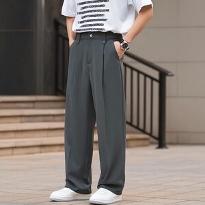 May include: Dark gray wide-leg trousers with a button closure and pockets. The pants are paired with white sneakers and a white t-shirt. The outfit is casual and stylish, suitable for everyday wear.