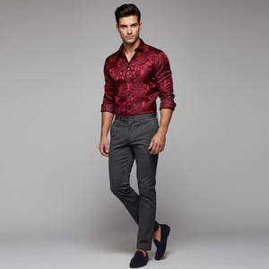 May include: A burgundy button-down shirt with a paisley pattern is paired with gray dress pants and navy blue loafers. The shirt has long sleeves and is unbuttoned at the top. The pants are a slim fit.