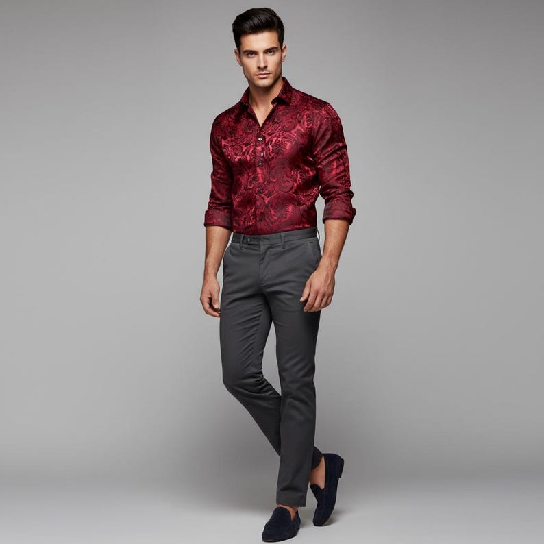 May include: A burgundy button-down shirt with a paisley pattern is paired with gray dress pants and navy blue loafers. The shirt has long sleeves and is unbuttoned at the top. The pants are a slim fit.