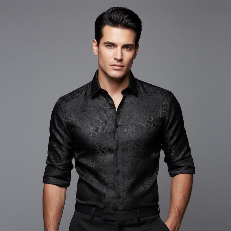 May include: A black button-down shirt with a paisley pattern. The shirt has long sleeves and a classic collar. The fabric has a subtle sheen, and the overall look is formal and stylish. The shirt is paired with black pants.