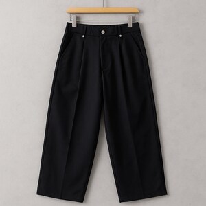 May include: Black wide-leg pants hanging on a wooden hanger. The pants have a high waist, pleats, and side pockets. The fabric appears to be a smooth, solid material. The pants are a classic, versatile garment.