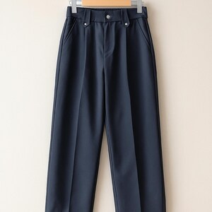 May include: Navy blue trousers hanging on a hanger. The pants have a high waist, a button closure, and two front pockets. The fabric appears to be a smooth, solid color. The trousers are a classic style, suitable for various occasions.