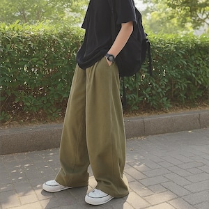 May include: Olive green wide-leg pants paired with a black t-shirt and white sneakers. A black backpack is worn over the shoulder. The outfit is casual and comfortable, suitable for everyday wear.