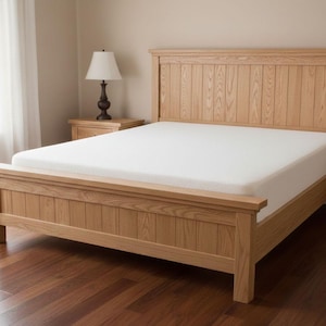 May include: A light-colored wooden bed frame with a matching headboard and footboard. The bed has a white mattress and is set in a room with a window and a bedside table with a lamp.