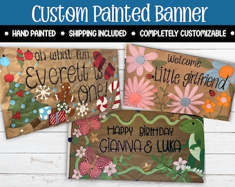 Puede incluir: Banners personalizados pintados a mano con texto e ilustraciones. Un banner dice "oh what fun Everett is one!" con arte temático navideño. Otro dice "Welcome Little girlfriend" con arte floral. Un tercer banner dice "Happy Birthday Gianna & Luka".