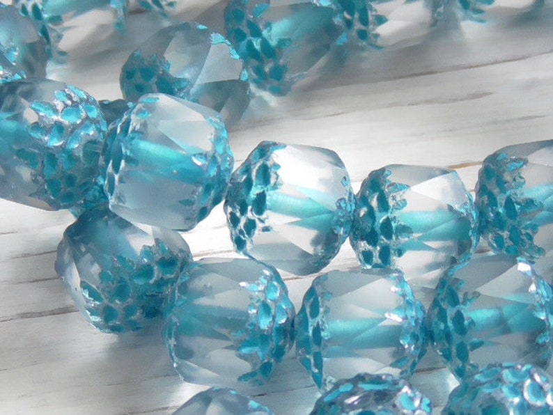 Pode incluir: Um fio de contas de vidro azul claro com acabamento texturizado e fosco. As contas s&atilde;o facetadas e t&ecirc;m um brilho sutil.