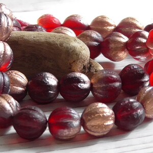 May include: A strand of red and gold glass beads. The beads are faceted and have a ribbed texture. The beads are strung on a wire and are arranged in a random pattern.