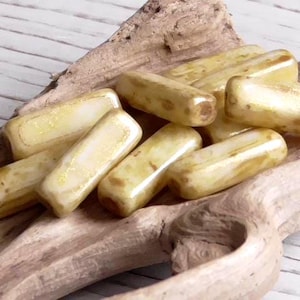 May include: A collection of rectangular, light yellow beads with a glossy finish. The beads are arranged on a piece of driftwood, showcasing their shape and color variations. These beads are ideal for jewelry making.