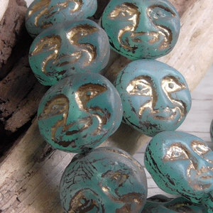 May include: A strand of turquoise blue glass beads with gold accents. Each bead is shaped like a face with a unique expression.