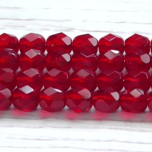 May include: A strand of red faceted glass beads. The beads are round and have a shiny finish.