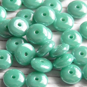 May include: A collection of teal green glass donut beads with a hole in the center. The beads are glossy and have a slight iridescent sheen.