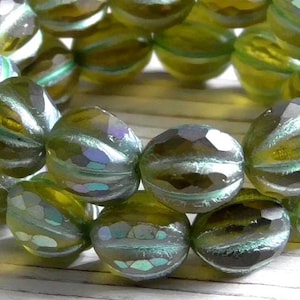 May include: Close-up of a strand of iridescent glass beads. The beads are faceted and have a mix of green, blue, and purple hues. The beads are round with a striped pattern and are arranged in a circular shape.