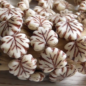May include: A strand of white glass beads with a brown leaf design. The beads are strung together and are ready to be used in a jewelry project.