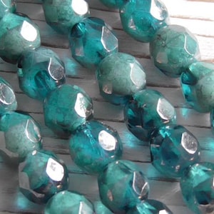 May include: A strand of teal blue faceted glass beads with a silver iridescent finish. The beads are strung on a clear thread.