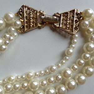 May include: A multi-strand pearl necklace with a gold-tone clasp in the shape of a bow. The pearls are white and round.
