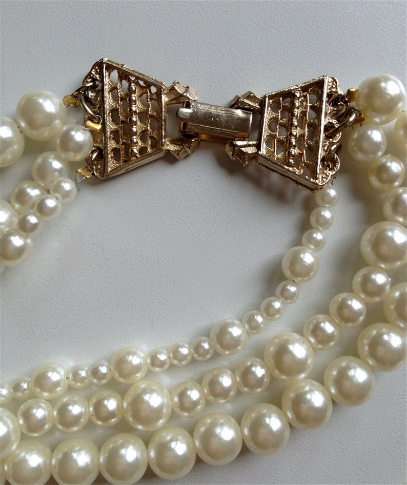May include: A multi-strand pearl necklace with a gold-tone clasp in the shape of a bow. The pearls are white and round.