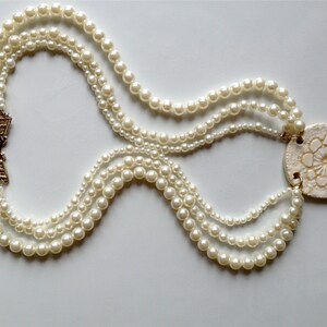 May include: A multi-strand pearl necklace with a gold clasp and a large white shell pendant with a floral design.