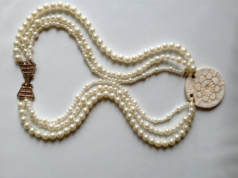 May include: A multi-strand pearl necklace with a gold clasp and a large white shell pendant with a floral design.