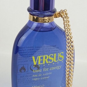 May include: A Versus eau de toilette bottle with a blue glass body and a dark blue cap. The bottle has a gold chain and a gold pendant with the Versace logo. The bottle contains 125ml or 4.2 fl oz.