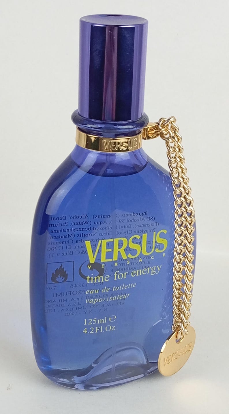 May include: A Versus eau de toilette bottle with a blue glass body and a dark blue cap. The bottle has a gold chain and a gold pendant with the Versace logo. The bottle contains 125ml or 4.2 fl oz.