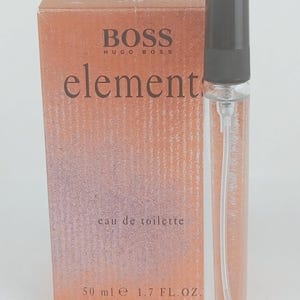 Puede incluir: Un frasco de perfume de vidrio transparente con tapón negro y pulverizador, junto a una caja naranja. La caja tiene las palabras "BOSS HUGO BOSS" y "element" impresas. La caja también dice "eau de toilette" y "50 ml e 1.7 FL.OZ."