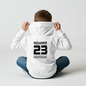 May include: A white hoodie featuring the name "RICHARD" and the number "23" in black on the back, with a black and white chequered flag design below. The person is wearing blue jeans.
