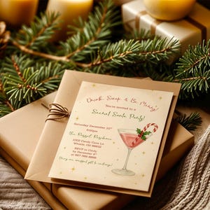 May include: A festive invitation for a Secret Santa party, featuring a cocktail illustration with a candy cane. The invitation is on a cream-colored card, with text in red and green, and is placed on top of wrapped gifts and greenery.