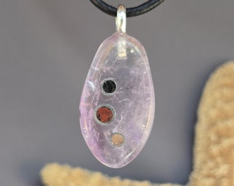 May include: A pink, oval-shaped pendant with three small, round, colorful stones set inside. The pendant is on a black leather cord.