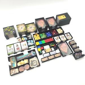 May include: A collection of black plastic game organizers, filled with various game components. The organizers hold cards, tokens, dice, and other game pieces. The game pieces are in various colors, including green, blue, red, yellow, and brown.
