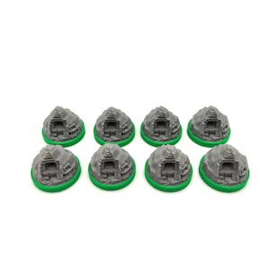 May include: Eight gray miniature temple models with green bases are arranged on a white surface. Each model features detailed architectural elements, resembling ancient structures. The models are designed for tabletop gaming or model building.
