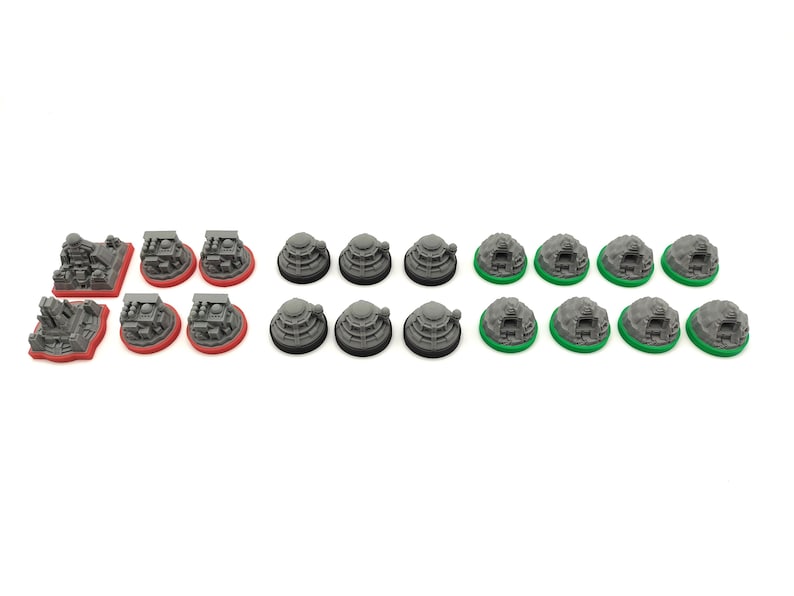 May include: A collection of miniature game pieces in various shapes and colors. There are gray structures with red bases, gray circular pieces with black bases, and gray structures with green bases. The pieces are arranged on a white background.