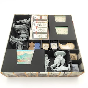 Puede incluir: Un organizador de juegos de mesa compartimentado con varias piezas de juego, incluyendo figuras en miniatura, cartas y fichas. El organizador es negro con un exterior decorativo y está diseñado para guardar todos los componentes del juego.
