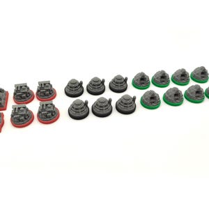 May include: A selection of miniature game pieces. The set includes grey structures with red bases, grey dome-shaped pieces, and grey rock-like pieces with green bases, all arranged on a white surface.