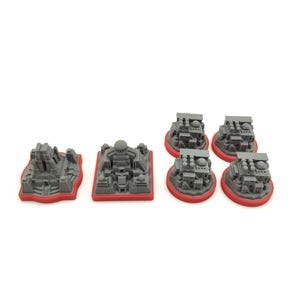 May include: A collection of gray miniature structures with red bases. The set includes various architectural designs, such as temples and buildings, suitable for tabletop gaming or model building. The pieces are made of a solid material.