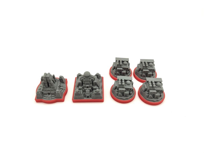 May include: A collection of gray miniature structures with red bases. The set includes various architectural designs, such as temples and buildings, suitable for tabletop gaming or model building. The pieces are made of a solid material.