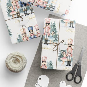 May include: Christmas-themed gift wrap featuring illustrations of nutcrackers and ballerinas. The presents are tied with twine and tags. A ball of twine, scissors, and blank tags are also visible. The wrapping paper has a festive design.
