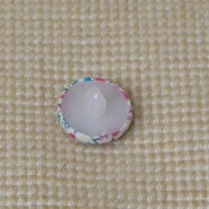 May include: A white button with a floral pattern in pink, blue, and green. The button has a clear plastic shank.