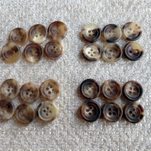 May include: A collection of 20 brown and beige buttons, each with four holes. The buttons are arranged in four rows of five buttons each.
