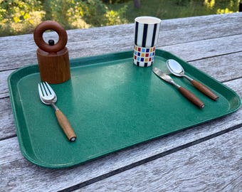 May include: A rectangular green serving tray featuring a wooden ring-topped pepper mill, a fork with a wooden handle, a knife with a wooden handle, a metal spoon with a wooden handle, and a cylindrical cup with black stripes and a colorful grid pattern.